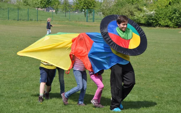 Betreuer und Kinder spielen auf der Wiese Try it (DE)